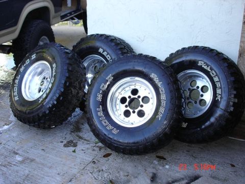 1985 Ford Bronco - Four Dick Cepek Radial M-T II tires on polished aluminum wheels are displayed on a concrete surface.