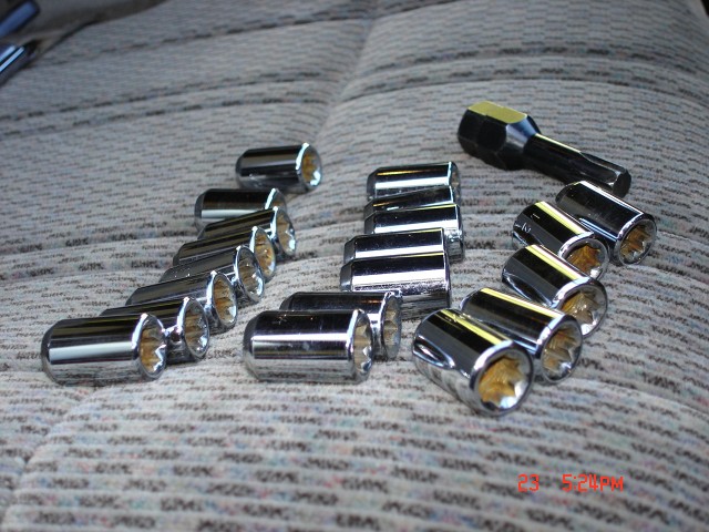 Several chrome lug nuts and a black socket wrench are laid out on a patterned fabric surface