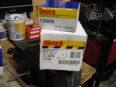 1992 Ford Bronco - Two Stant boxes for auto cooling parts sit on a workbench: a blue-and-yellow thermostat box marked '13008' and a white box for a water outl…