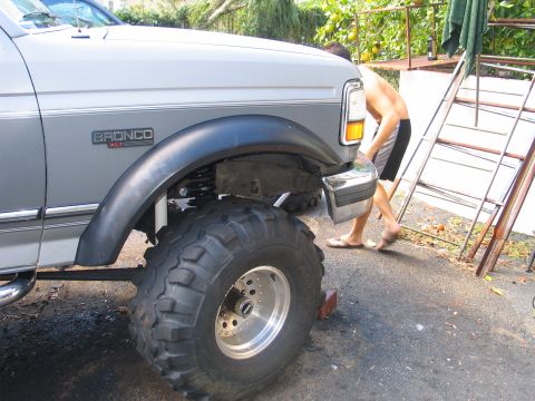 1992 Ford Bronco - Close side view of a white-over-gray Ford Bronco XLT front fender with a black flare, showing a tall lift with exposed coil spring and an o…