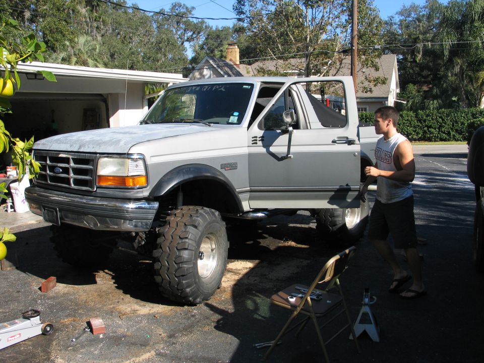 White lifted Ford Bronco on driveway with man working, large off-road tires and open door