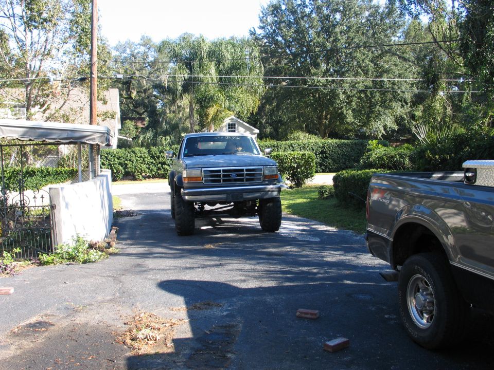 Lifted light gray 1990s Ford with oversized tires facing the camera in a palm-lined driveway