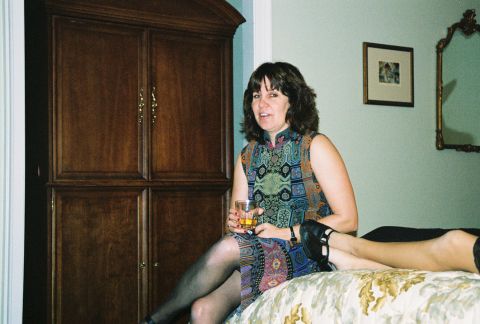 1994 Ford Bronco - A woman sits on a bed holding a drink, with a large wooden cabinet in the background and a mirror on the wall.