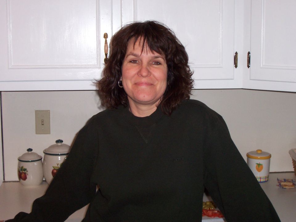 Woman in a dark sweater stands in a kitchen with white cabinets and countertop