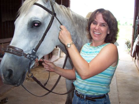 1994 Ford Bronco - A woman smiles while adjusting the bridle on a white horse inside a stable.