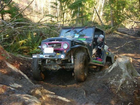 1990 Ford Bronco - Off-road vehicle tackling a challenging muddy terrain with large tires and a modified body.