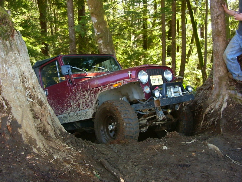 Maroon Jeep CJ-7 stuck between trees on a muddy trail
