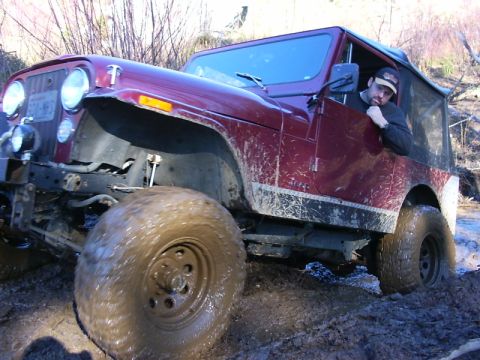 1990 Ford Bronco - A maroon Jeep CJ-7 navigates a muddy off-road trail with a driver visible.