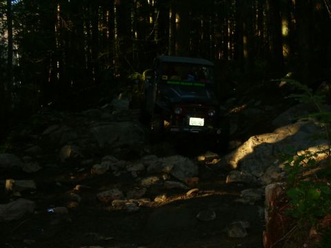 1990 Ford Bronco - A vehicle drives through a challenging, rocky path in a dark forest.