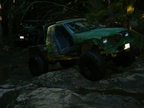 1990 Ford Bronco - A modified green truck navigates a challenging rocky path in a wooded area.