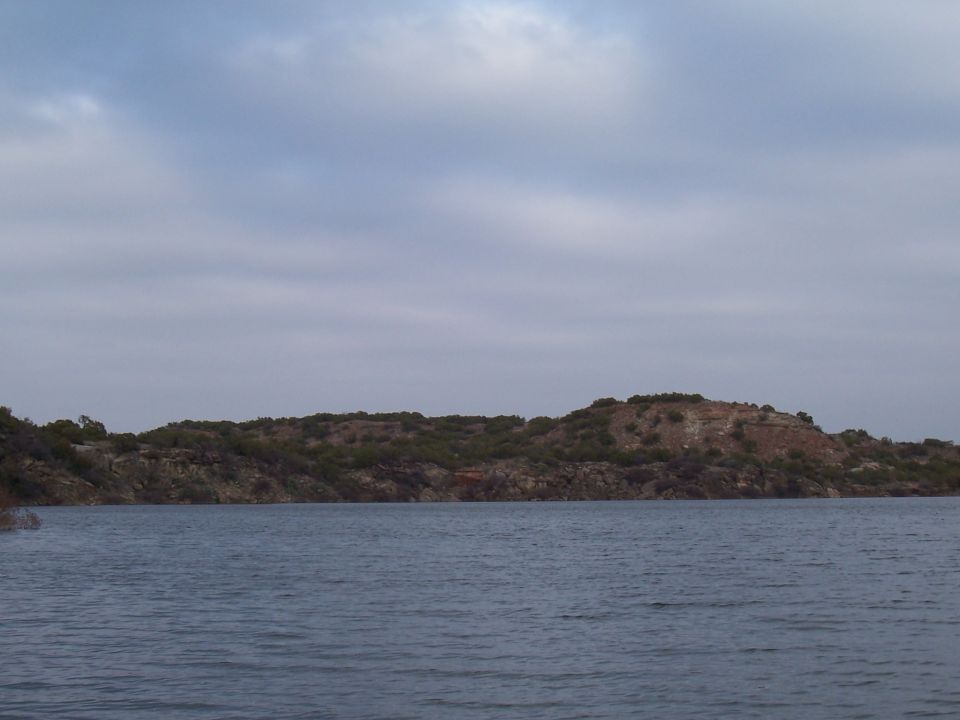 Choppy lake water below a rocky brush-topped bluff under a cloudy sky