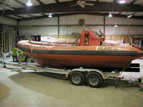 1988 Ford Bronco - An orange inflatable boat with a red console sits on a trailer in a large garage.
