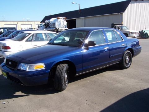 2001 Ford Crown Victoria - A blue 2001 Ford Crown Victoria is parked in a lot next to other vehicles.