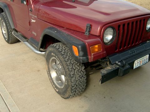 1998 Jeep TJ - Front view of a red 1998 Jeep TJ, showing the fender, tire, and grille. The license plate is visible.