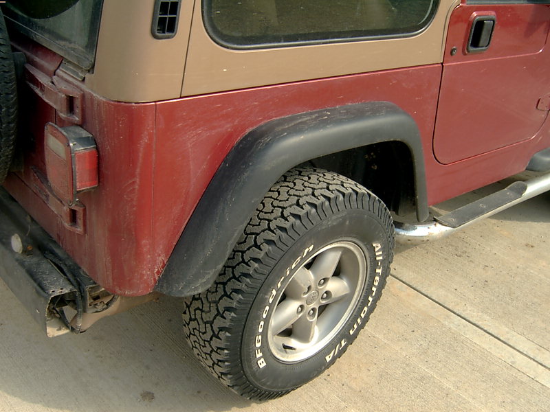 Red and tan Jeep Wrangler rear quarter panel, fender, and tire. Visible "All-Terrain T/A" text on tire