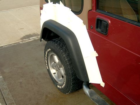 1998 Jeep TJ - A red Jeep's rear fender is covered in masking tape, preparing for a paint job.