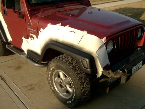 1998 Jeep TJ - A red Jeep Wrangler is partially masked with white tape on its front fender and hood, suggesting preparation for painting.