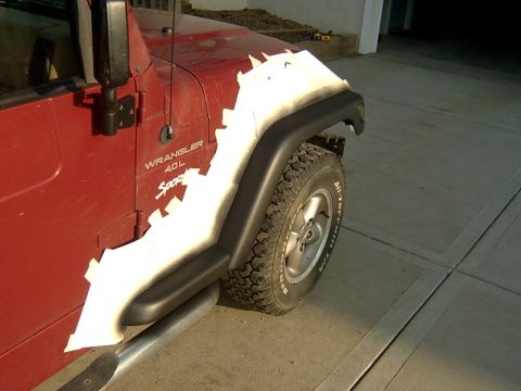 1998 Jeep TJ - A red 1998 Jeep Wrangler is shown from the side, white tape applied in a jagged pattern to the front fender.