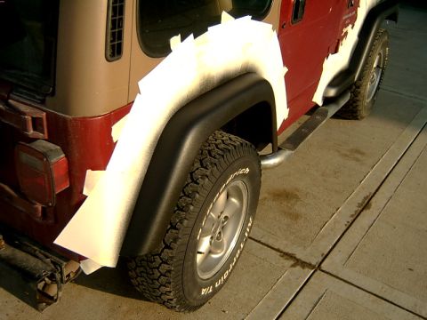 1998 Jeep TJ - The rear fender of a Jeep is covered in tape and paper, likely in preparation for bodywork or paint work.