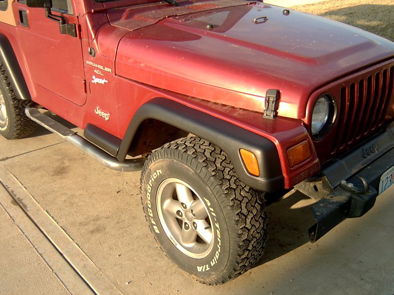 Red Jeep Wrangler with side steps and BFGoodrich All-Terrain tires. Front fender and hood visible