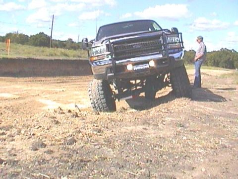 1989 Ford Bronco - A lifted Ford F-Series truck is positioned on a dirt mound with a person standing nearby.