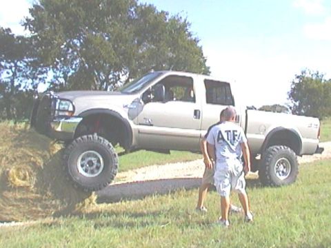 1989 Ford Bronco - Pickup truck with lifted suspension and large off-road tires is positioned on a grassy slope.