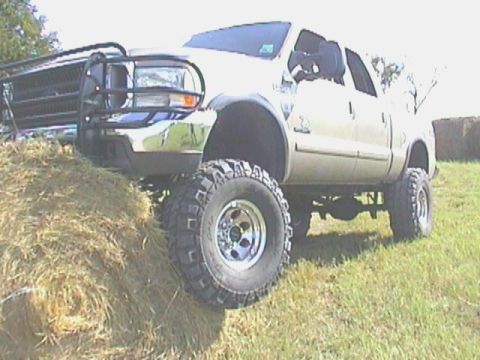 1989 Ford Bronco - A lifted pickup truck is positioned on a large hay bale in a grassy field.
