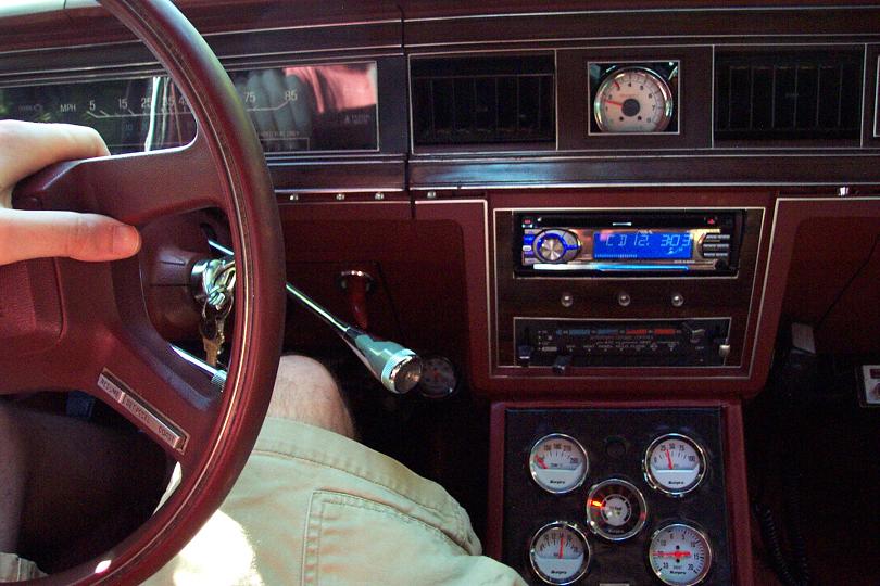 Car interior showing steering wheel, dashboard with radio, and gauges. The dashboard has woodgrain trim