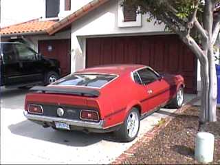 1971 Ford Mustang - A red 1971 Ford Mustang is parked in front of a garage, with a black truck visible to the left.