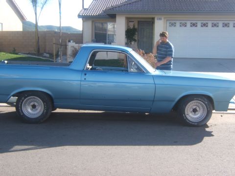 1967 Ford Ranchero - A light blue 1967 Ford Ranchero pickup truck is parked in front of a house with a man standing beside it.