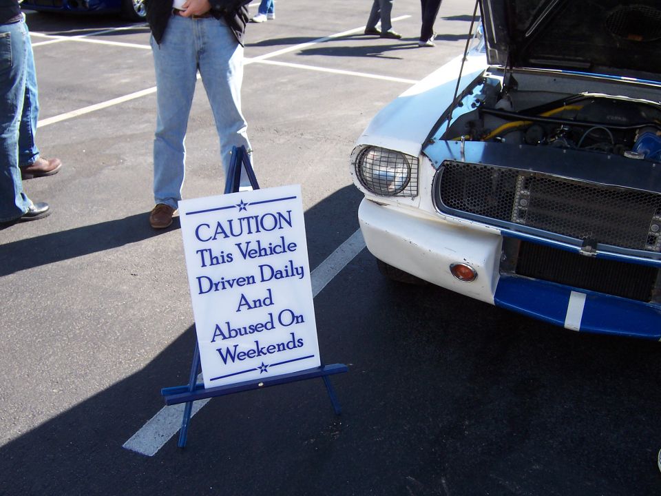 White classic car with blue racing stripes, hood open, parked next to a caution sign