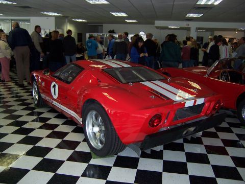1971 Ford Mustang - A red race car with white stripes and the number 1 is displayed indoors on a checkered floor, with another red car visible to the right.