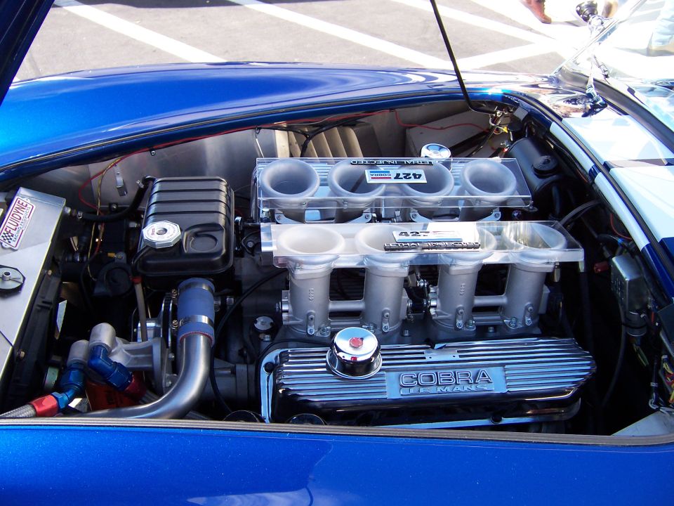 Close-up of a blue Shelby Cobra's V8 engine with "COBRA 427" visible on the valve covers and intake manifold