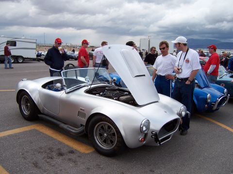 1971 Ford Mustang - Silver AC Cobra on display with hood open, showing the engine. Another blue Cobra is visible behind it.