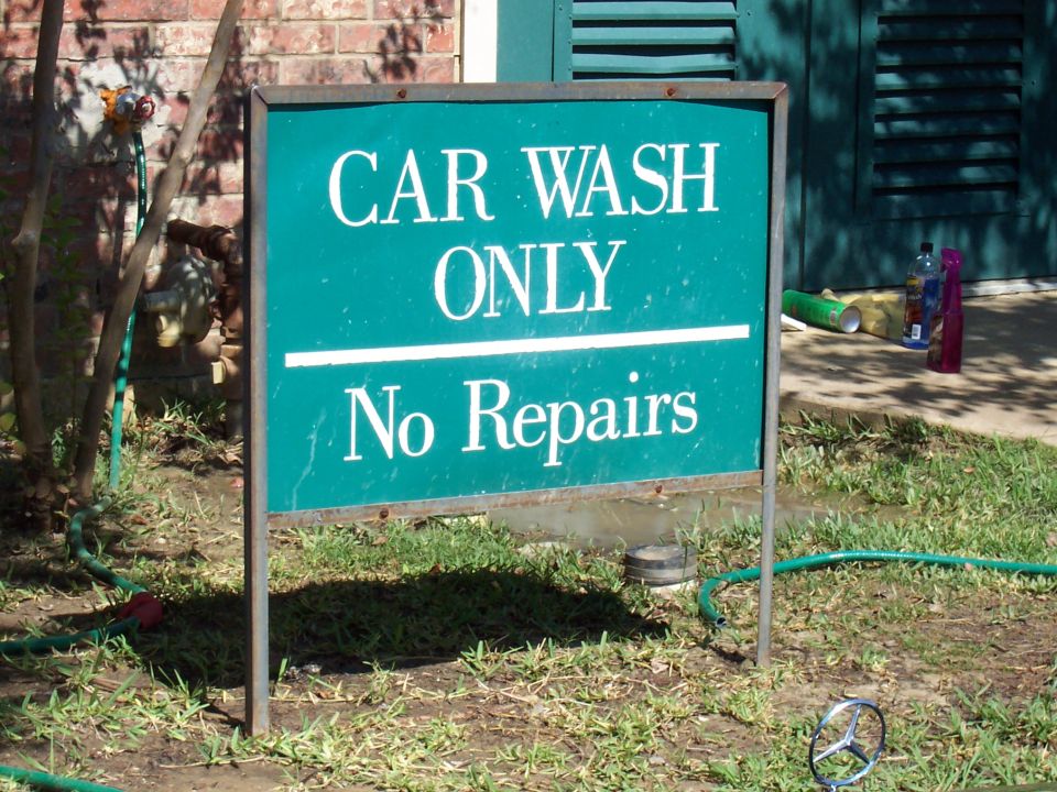 Green metal yard sign reading CAR WASH ONLY No Repairs in front of a brick wall and hose