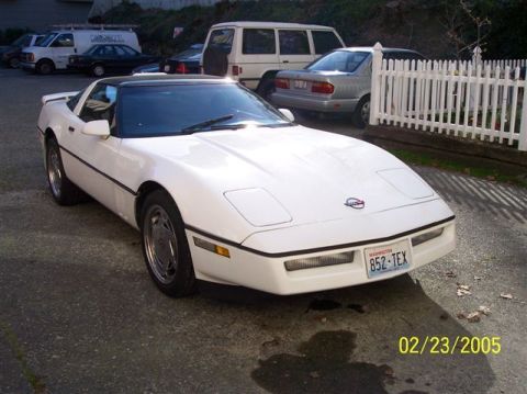 1994 Ford Bronco - A white Chevrolet Corvette is parked in a driveway with other vehicles visible in the background.