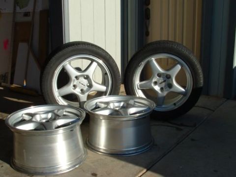 1994 Ford Bronco - A set of four aftermarket wheels are displayed outside a garage door.