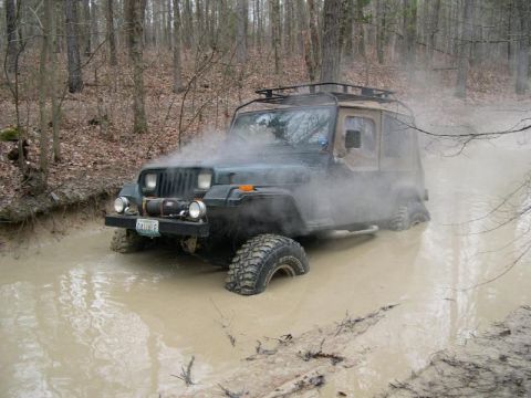 1999 Jeep TJ - This Jeep Wrangler YJ is navigating a muddy trail, with steam rising from the engine area.