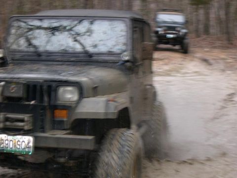 1999 Jeep TJ - Two Jeeps navigate a muddy off-road path in a wooded area.
