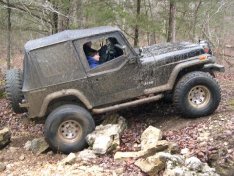1999 Jeep TJ - A black Jeep Wrangler navigates a rocky trail with a soft top and mud splattered on its body.