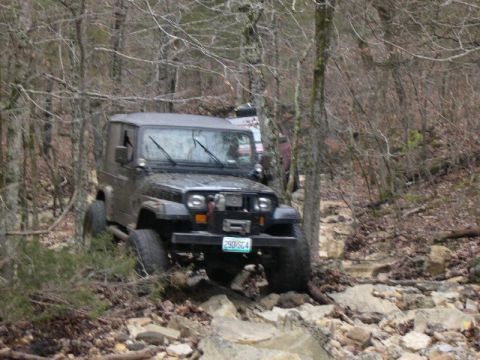 1999 Jeep TJ - A Jeep Wrangler navigates a rocky off-road trail surrounded by trees.