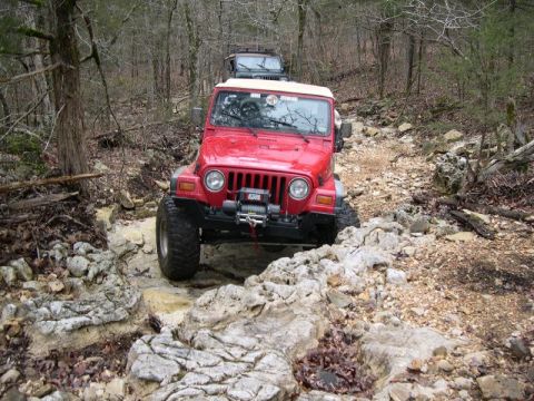 1999 Jeep TJ - Two Jeeps tackle a challenging, rocky off-road path through a wooded area.