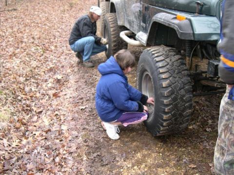 1999 Jeep TJ - Two people attend to the tires of a green Jeep off-road.
