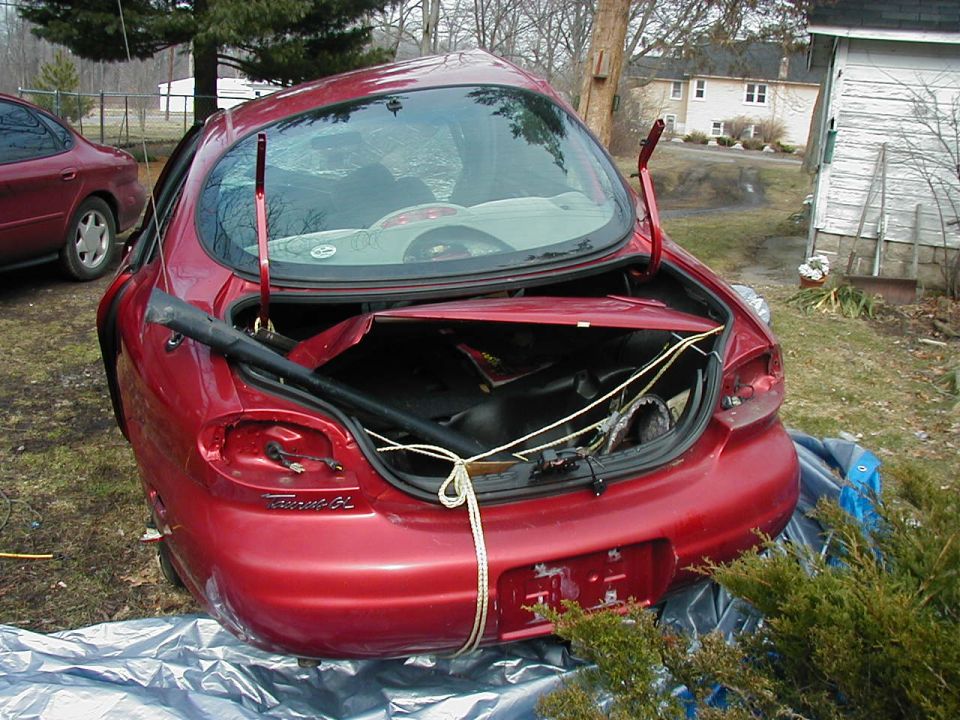Red 1997 Ford Taurus with trunk open, showing damage and contents. Another red car is parked nearby