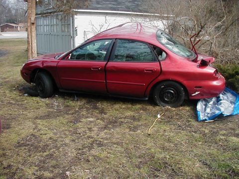 1997 Ford Taurus - This red sedan appears to have sustained significant damage to its front and rear, with the trunk left ajar.