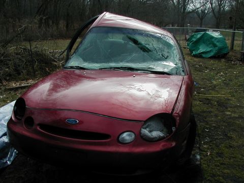 1997 Ford Taurus - This red 1997 Ford Taurus has a severely damaged roof and front end, with one headlight missing.
