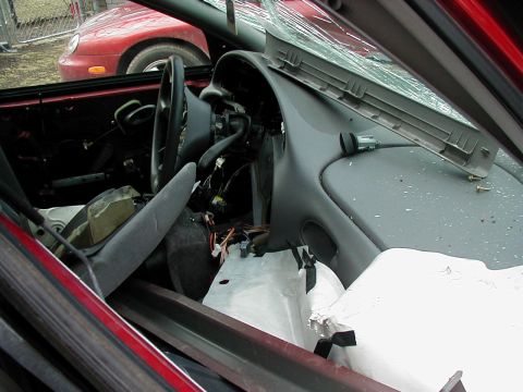 1997 Ford Taurus - The interior of a damaged red car shows a cracked windshield and exposed wiring, with another red vehicle in the background.