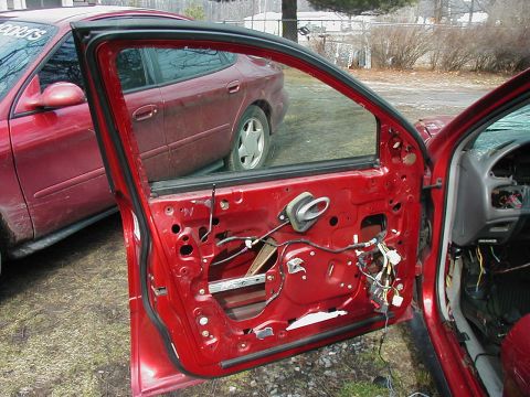 1997 Ford Taurus - The interior of a red car's door is exposed, revealing wiring and mechanisms, with another vehicle visible in the background.