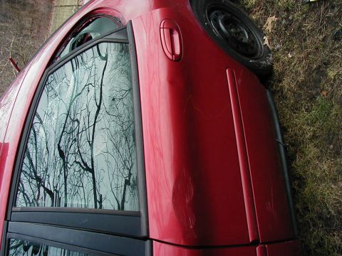 1997 Ford Taurus - Side view of a red car's door and window, showing reflections and body damage.