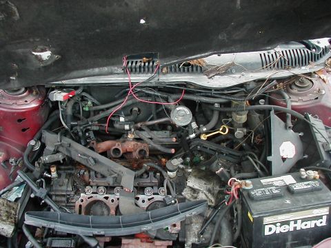 1997 Ford Taurus - The engine bay of a vehicle, showing the engine block, battery, and various hoses and wires. The hood is open.